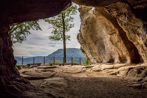 Blick aus einer Höhle auf eine Landschaft mit Bäumen und einem Berg im Hintergrund.