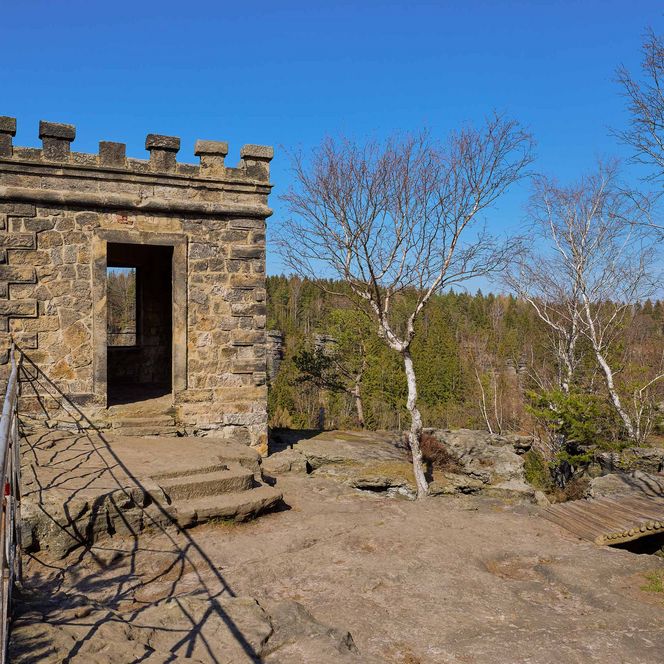 Steinerne Ruine mit Tür, umgeben von Bäumen und blauem Himmel im Bielatal