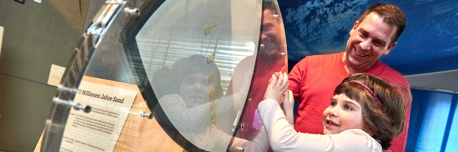 Vater und Tochter interagieren mit einem großen, runden Objekt in einem Ausstellungsraum.