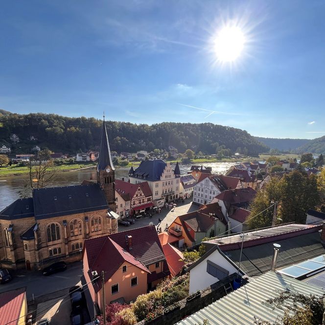 Blick auf eine malerische Stadt mit bunten Häusern, umgeben von Hügeln und einem Fluss unter klarem Himmel.