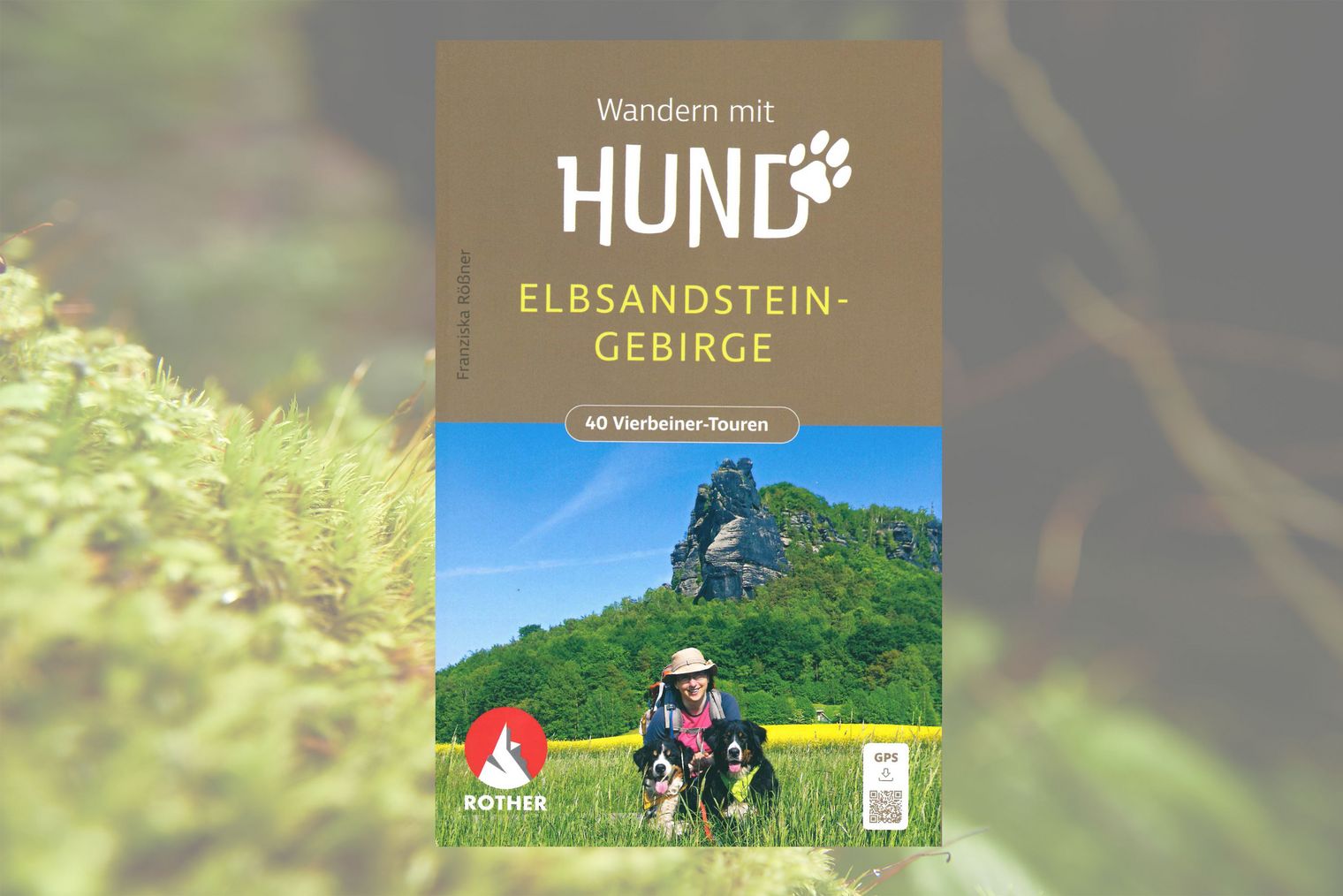 Wanderbuch mit dem Titel "Wandern mit Hund" und einem Bild von einer Person mit zwei Hunden in der Wiese sitzend, im Hintergrund Wald und Felsen.