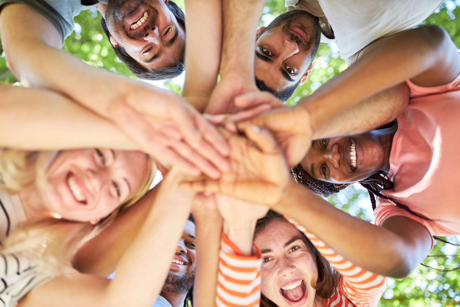 Gruppe junger Leute Sechs Personen mit lächelnden Gesichtern legen ihre Hände übereinander in die Mitte.