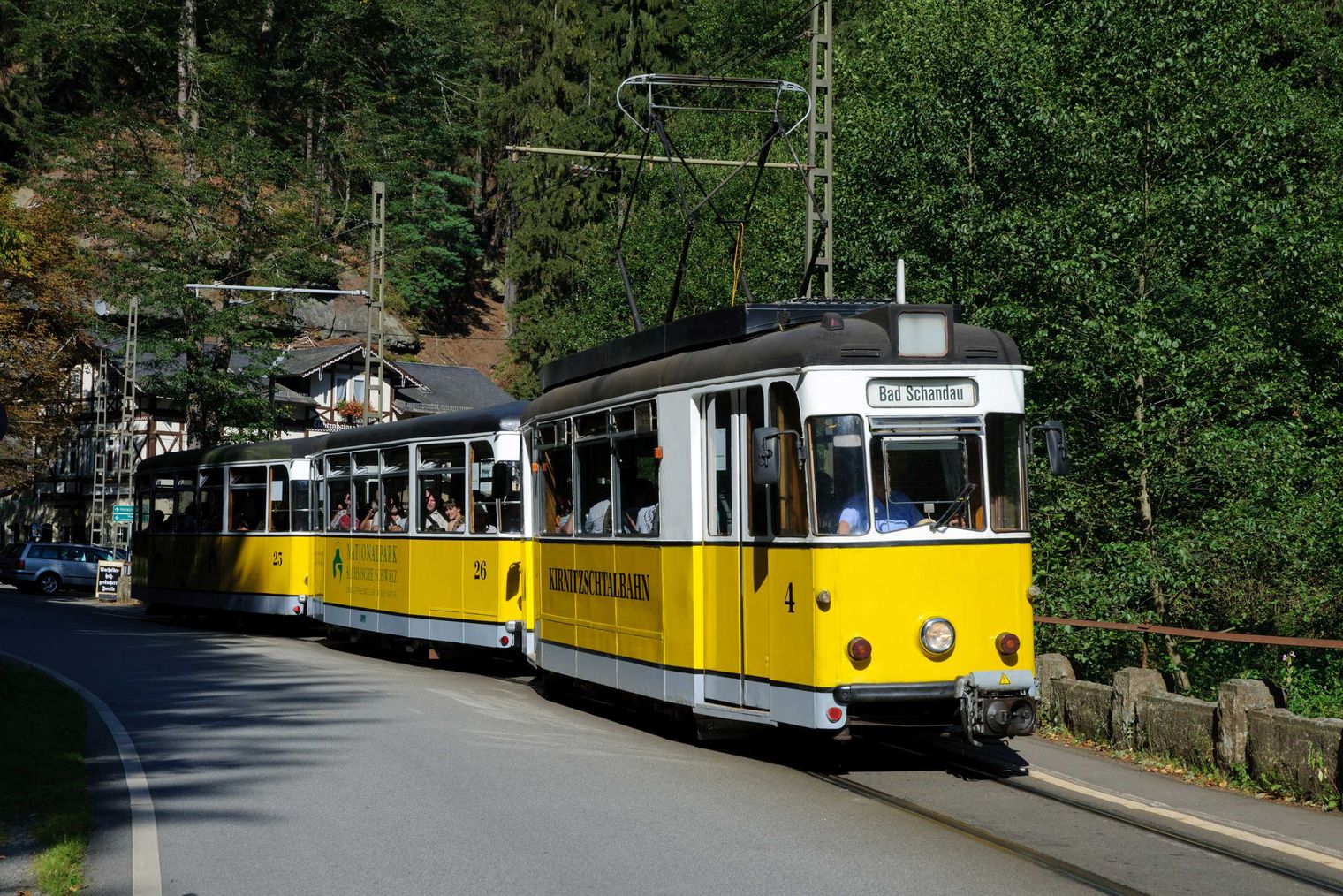 Gelbe historische Straßenbahn fährt auf Schienen durch grünen Wald.