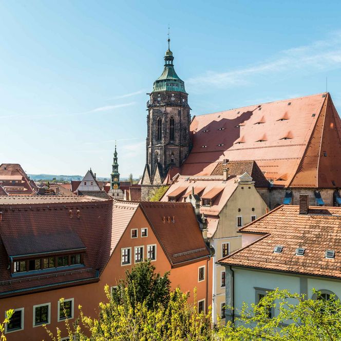 Blick auf ein Stadtbild mit roten Dächern und einem Kirchturm unter blauem Himmel.