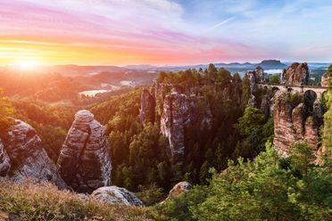 Sonnenuntergang über einem dicht bewaldeten und felsigem Gebiet mit farbenfrohem Himmel.