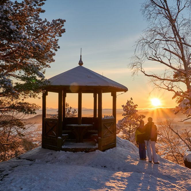 Winterlandschaft mit einem Pavillon, Schnee, Bäume und Sonnenuntergang im Hintergrund.