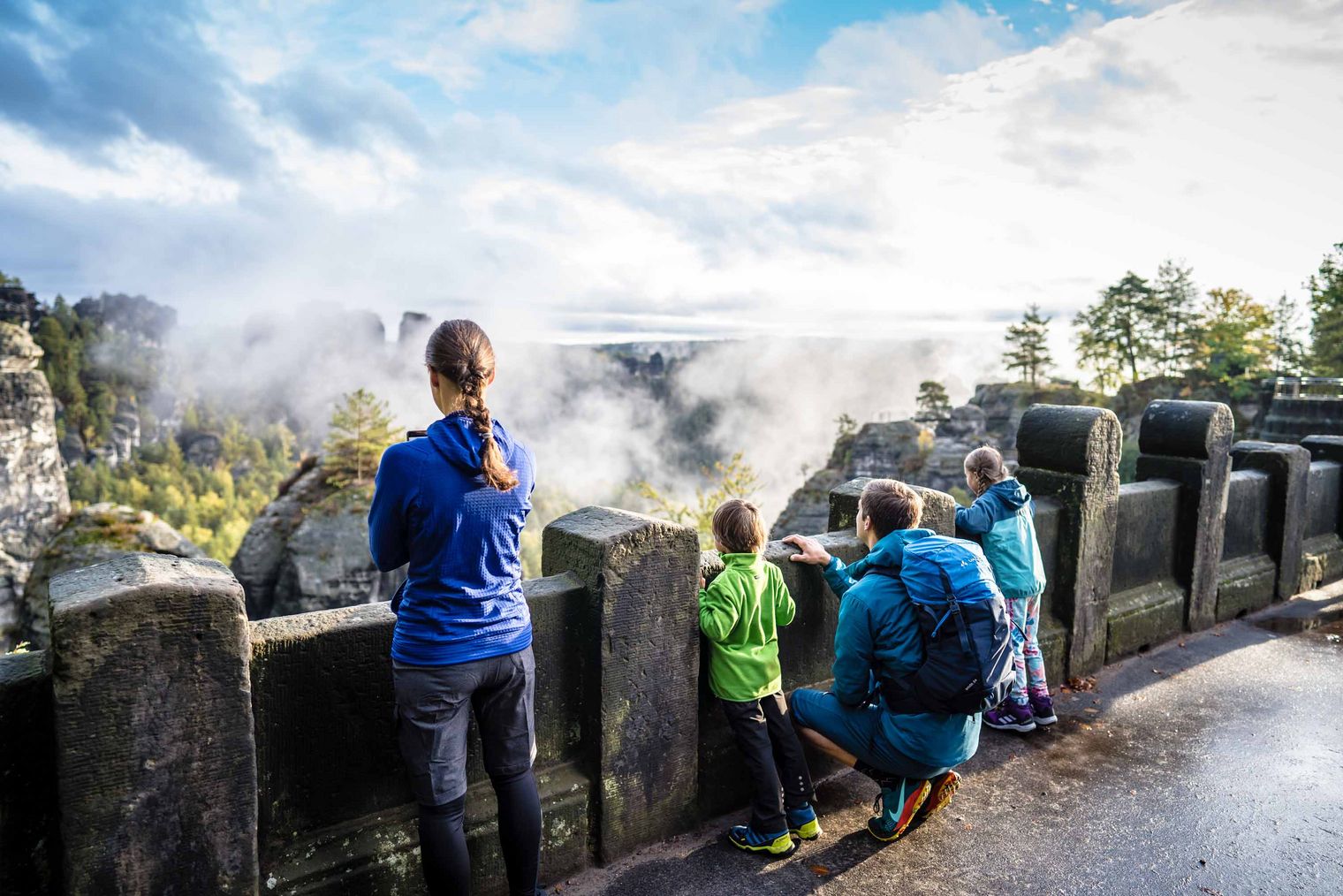 Familie steht an der Basteibrücke und blickt auf eine neblige Landschaft.