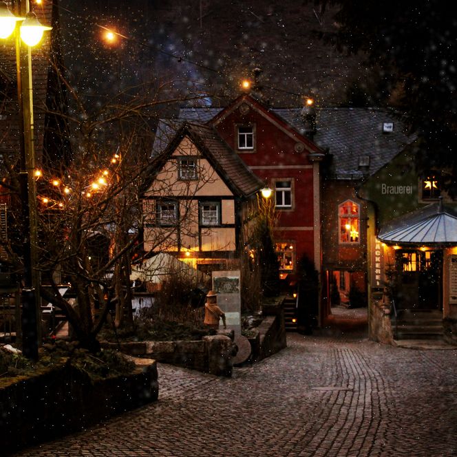 Winterliche Straße mit schneebedeckten Häusern und warmem Licht von Laternen.