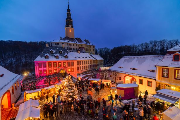 Schloss mit Beleuchtung und Weihnachtsmarktständen bei Dämmerung.