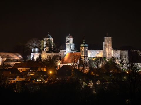 Burg Stolpen bei Nacht, beleuchtet und umgeben von Sternenhimmel.