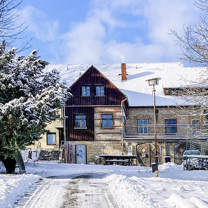 Zweistöckiges Haus mit Schnee bedeckt, umgeben von schneebedeckten Bäumen und einem klaren blauen Himmel.