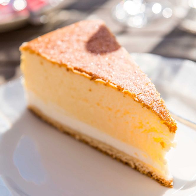Ein Stück Käsekuchen auf einem weißen Teller, mit goldbrauner Kruste und cremiger Füllung.
