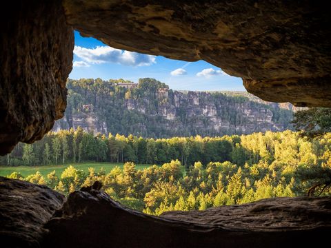 Blick durch Felsen auf die Bastei, im Vordergrund Wälder und grüne Wiesen.