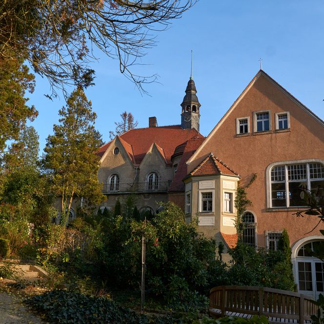 Schloss Thürmsdorf mit roten Dächern, umgeben von Bäumen und einem Weg im Vordergrund.