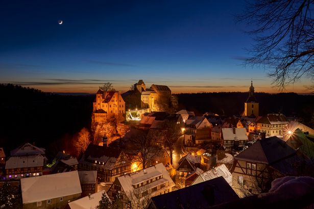 Schneelandschaft mit Burg Hohnstein auf einem Hügel bei Abend. 