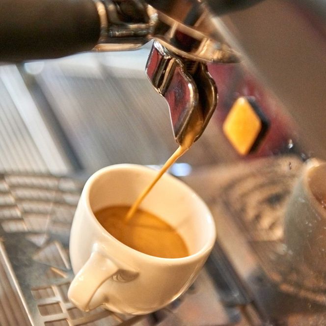 Espresso fließt aus einer Kaffeemaschine in eine weiße Tasse.