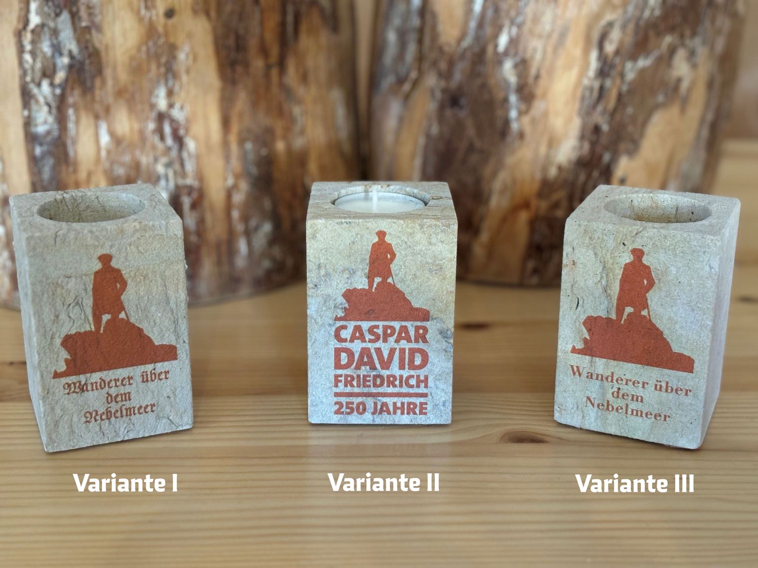 Auf einem Holztisch stehen drei Teelichthalter aus Sandstein mit verschiedenen roten Aufdrucken.