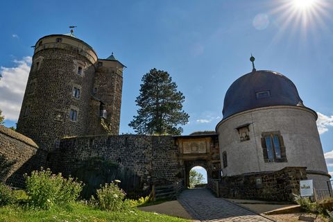 Zwei historische Türme der Burg Stolpen mit Kuppel und Tor, umgeben von grünem Gras und blauen Himmel.