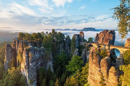 Felsenlandschaft mit grünen Bäumen und einem Himmel voller Wolken und Sonnenlicht.