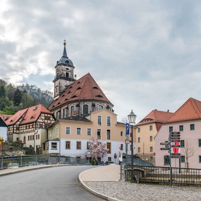 Fachwerkhäuser mit roten Dächern und einer Kirche im Hintergrund unter bewölktem Himmel.