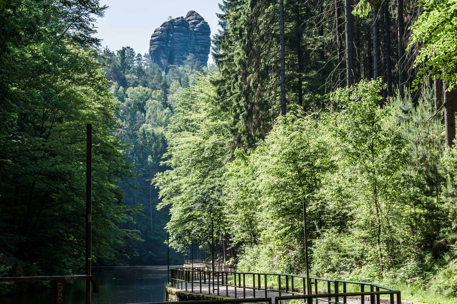 Amselsee umgeben von grünem Wald mit markanten Rathener Felsformation im Hintergrund