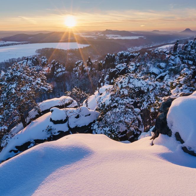 Sonnenaufgang über schneebedeckten Felsen der Schrammsteine mit Blick in die winterlichen Landschaft des Elbtals