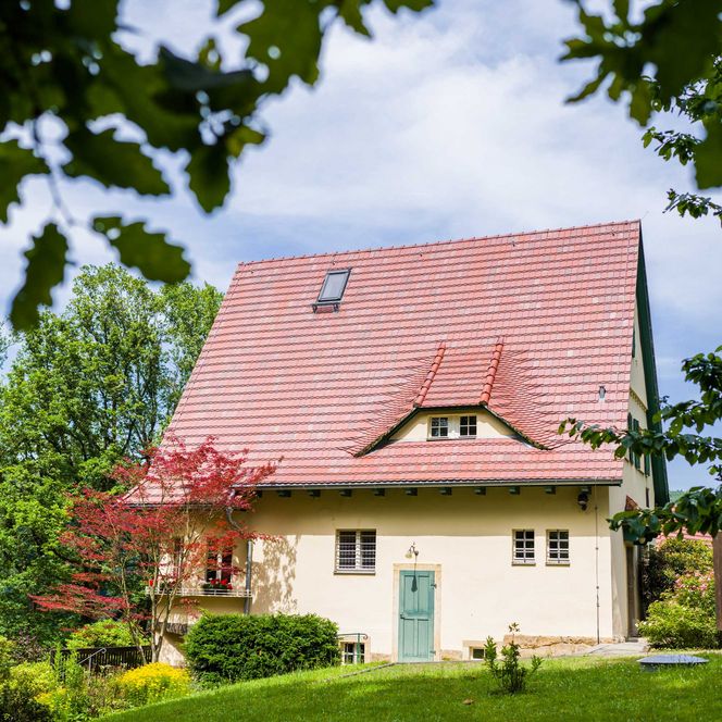 Haus des Malers Robert Sterl mit rotem Satteldach, umgeben von Bäumen und einem gepflegten Garten.