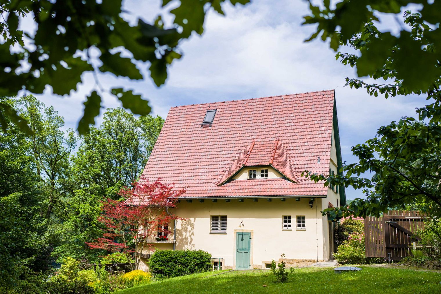 Haus des Malers Robert Sterl mit rotem Satteldach, umgeben von Bäumen und einem gepflegten Garten.