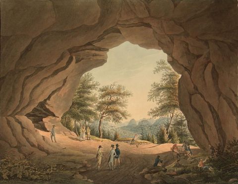 Blick aus einer Höhle auf eine Landschaft mit Bäumen und Bergen im Hintergrund, Menschen stehen im Vordergrund.