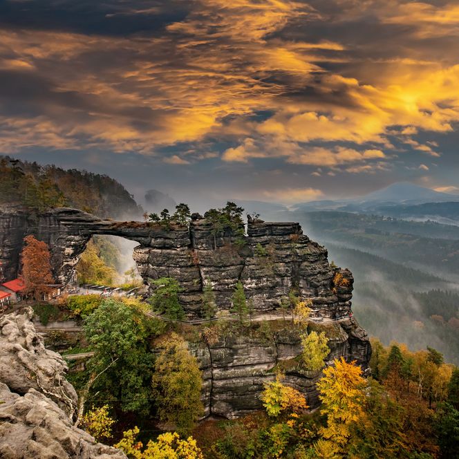 Blick auf ein Felsentor mit buntem Herbstlaub und dramatischem Himmel.