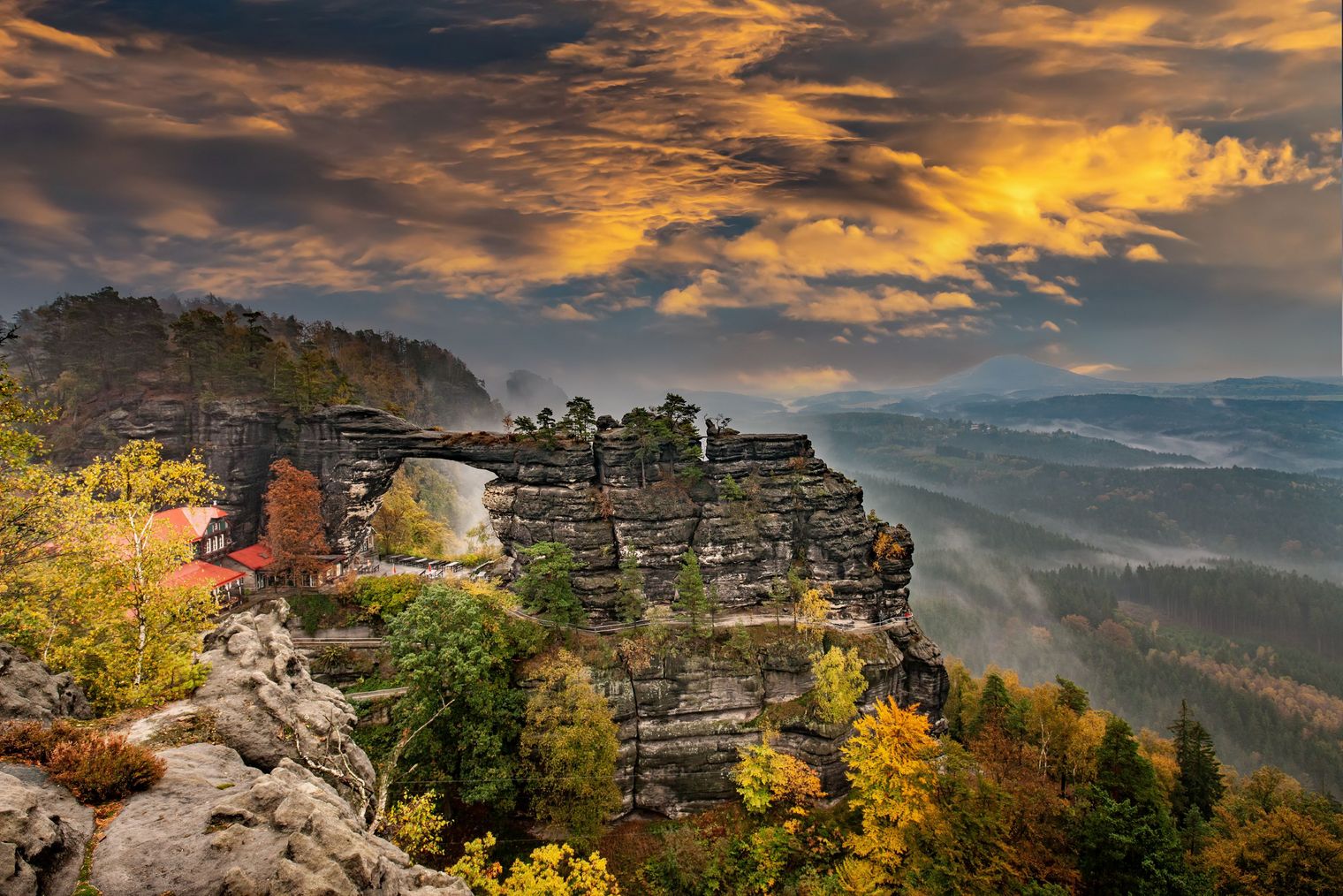 Blick auf ein Felsentor mit buntem Herbstlaub und dramatischem Himmel.