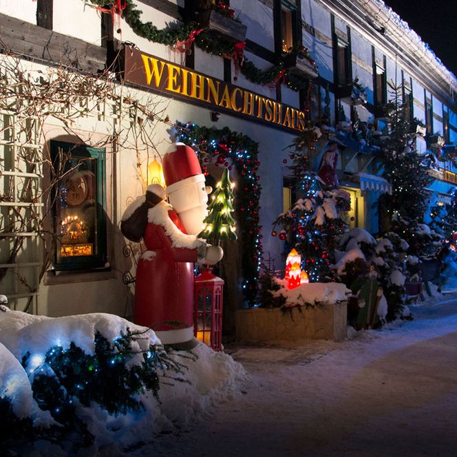Weihnachtlich dekorierte Straße mit einem großen Weihnachtsmann und schneebedeckten Bäumen.