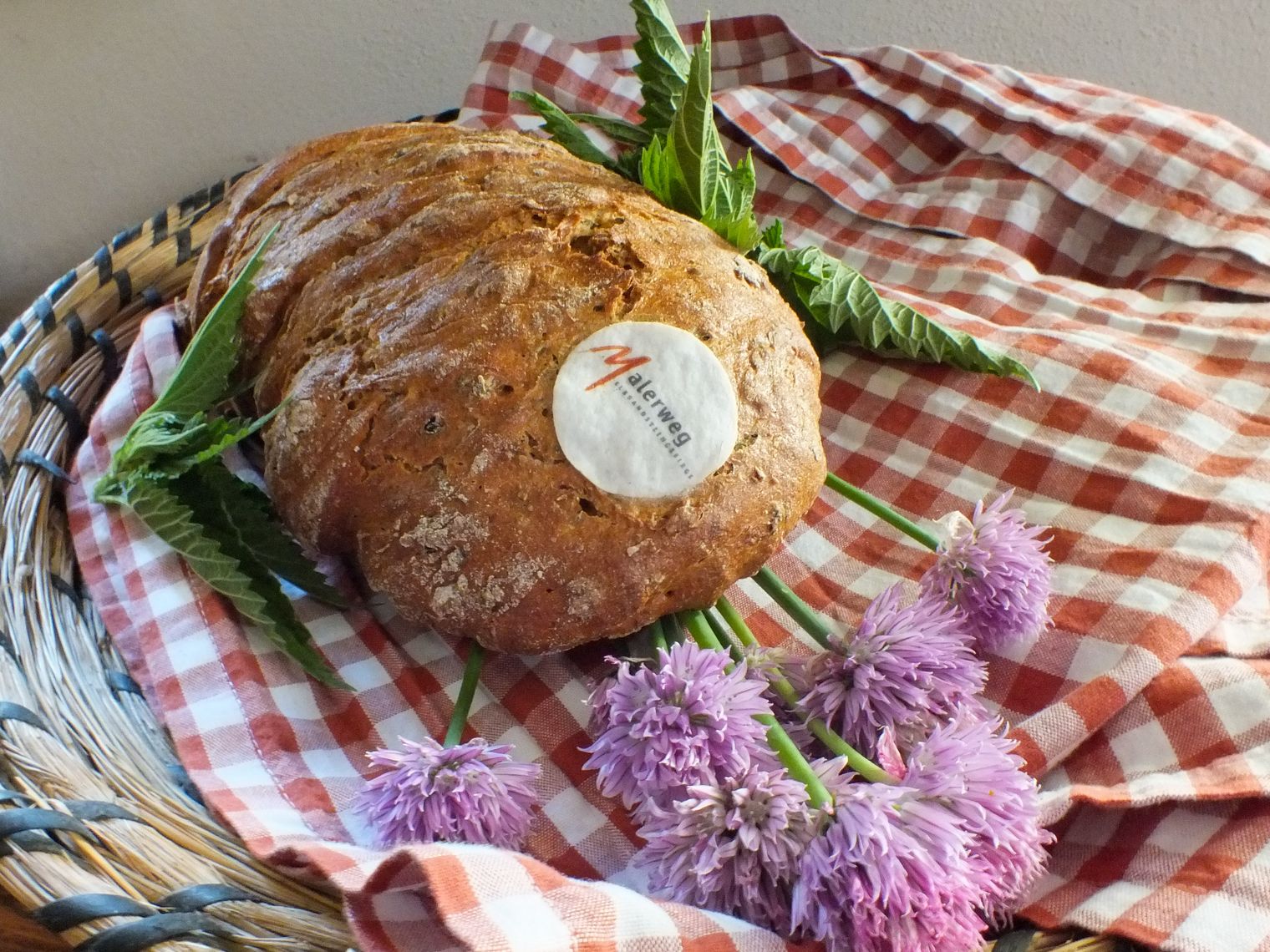 Ein Laib dunkles, frisches, knuspriges Brot liegt auf einer weiß-rot-karierten Decke.