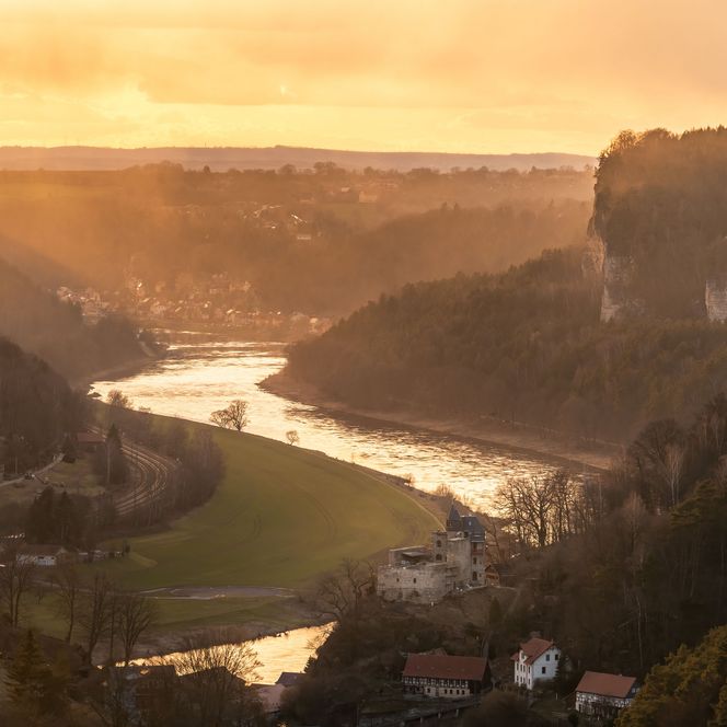 Sonnenuntergang über einem Fluss, umgeben von Hügeln und Wäldern.