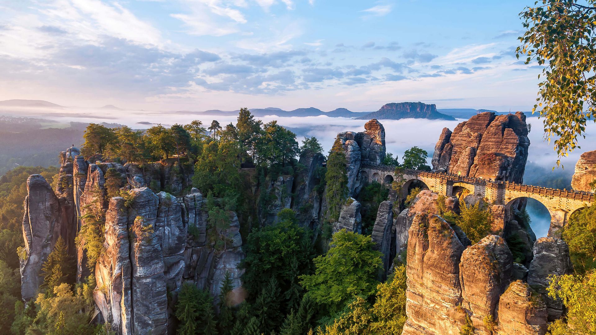 Felsenlandschaft mit grünen Bäumen und Wolken im Hintergrund, bei Sonnenaufgang.