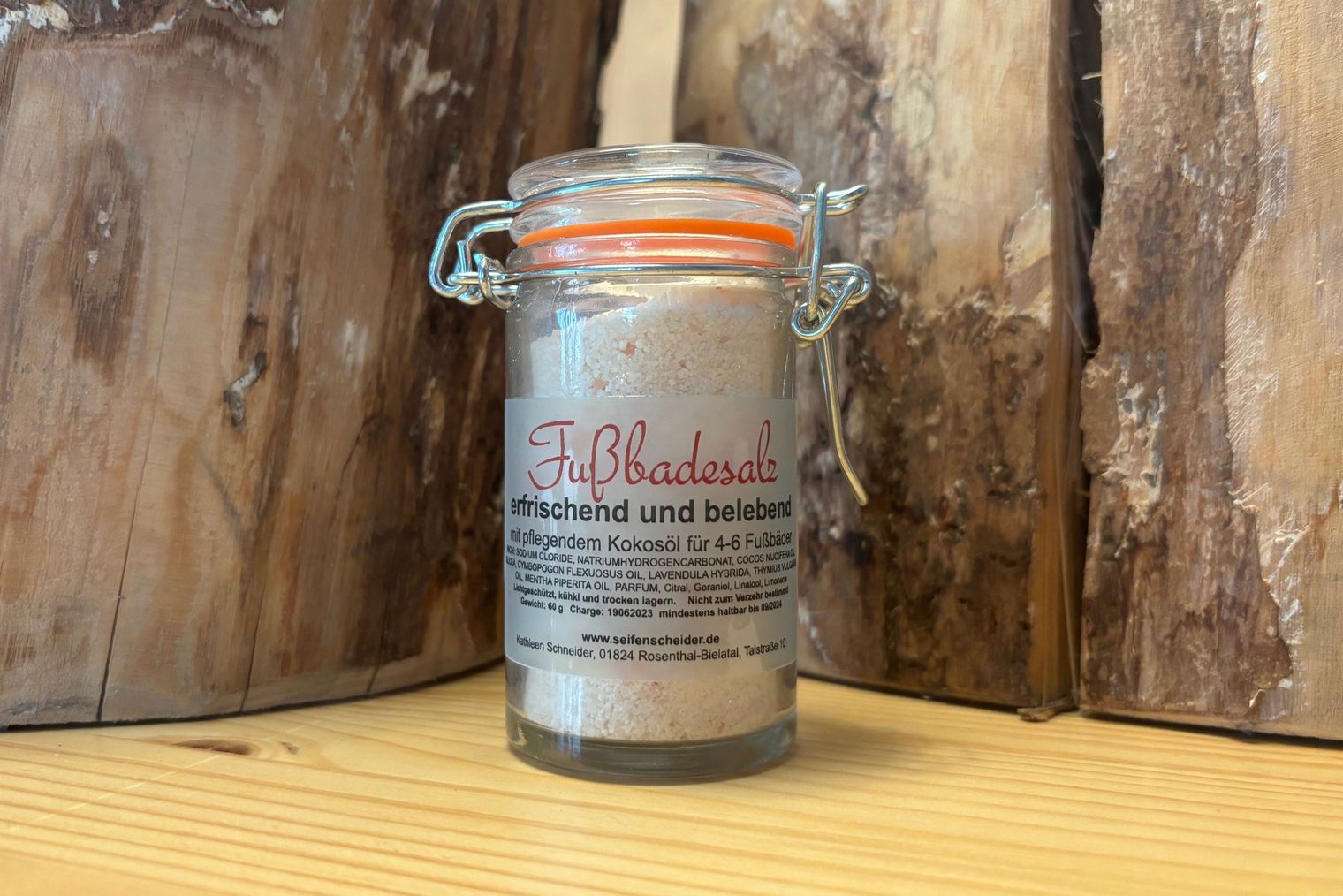Glas mit Badesalz gefüllt und einem orangefarbenen Deckel, auf einem Holztisch vor einem Holzstamm.
