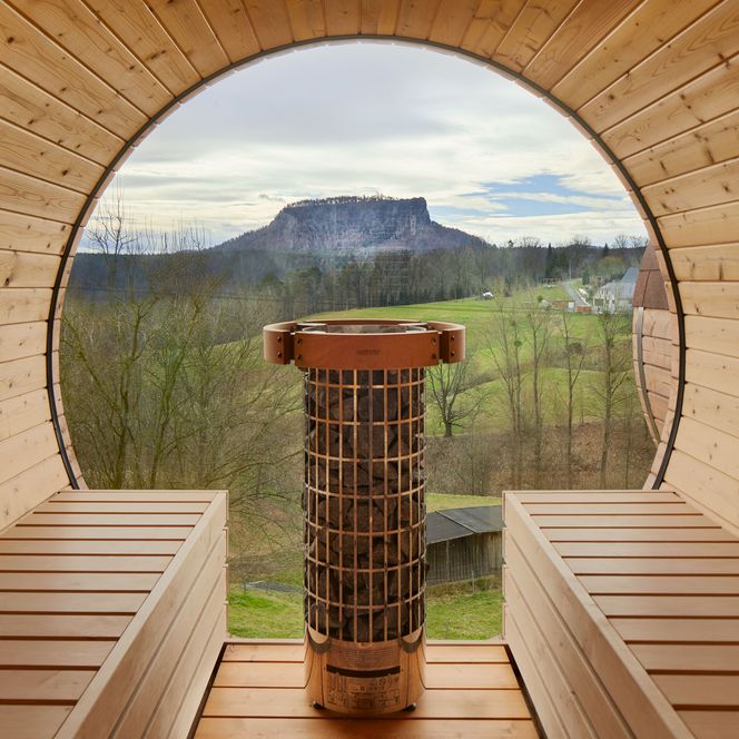 Blick aus einer Holzsauna auf eine grüne Landschaft mit einem Berg im Hintergrund.