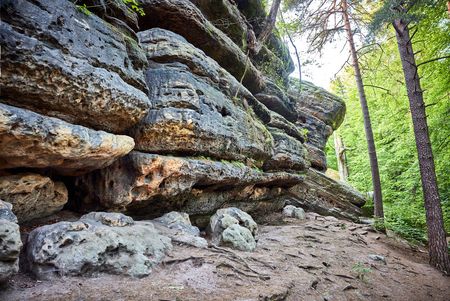 Felsformation mit schichtartigen Strukturen, umgeben von grünen Bäumen und einem schmalen Weg.