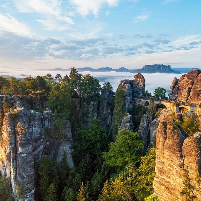 Felsenlandschaft mit grünen Bäumen und einem Himmel voller Wolken und Sonnenlicht.