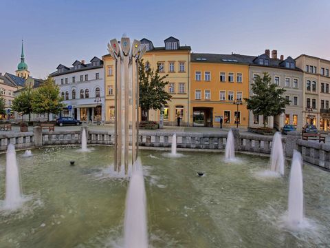 Marktplatz in Sebnitz mit Brunnen, bunten Gebäuden, und bewölktem Himmel.