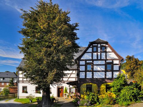 Umgebindehaus in Hinterhermsdorf mit weißer Fassade und bunten Blumen im Garten. blauer Himmel im Hintergrund.