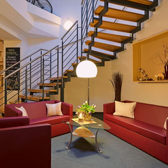 Rote Sofas mit Kissen, Glastisch und Stehlampe in einem modernen Raum mit Treppe im Hintergrund.