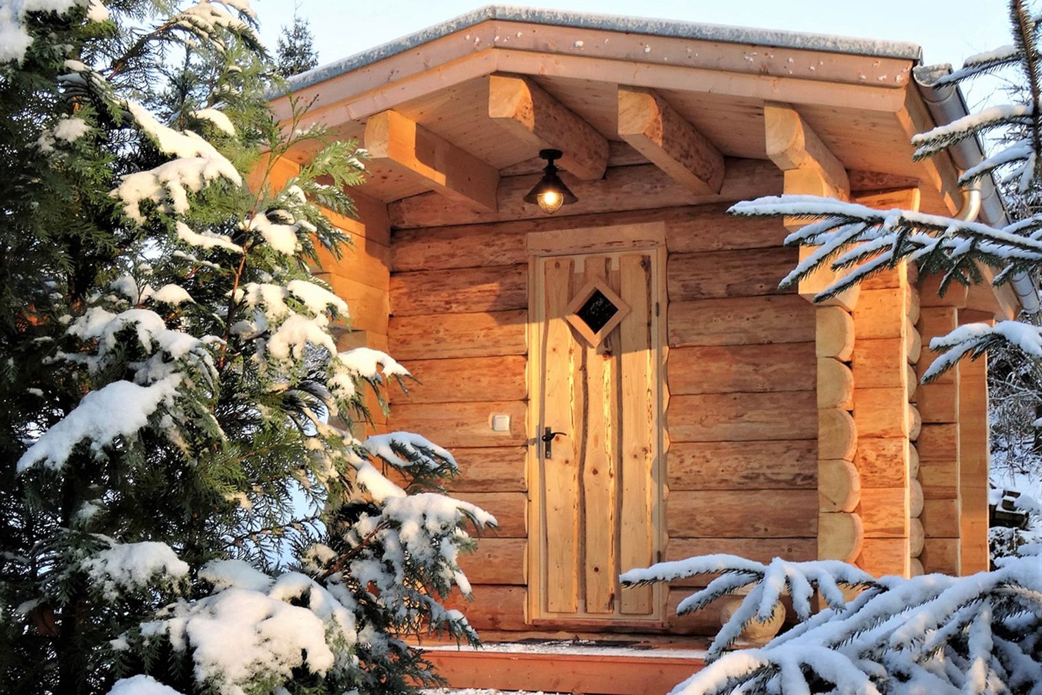 Holzhütte mit einem spitzen Dach, umgeben von schneebedeckten Bäumen.
