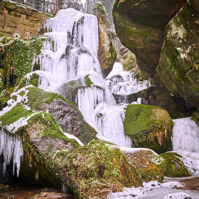Eisige Wasserfälle fließen über moosbedeckte Felsen in einer felsigen Umgebung.
