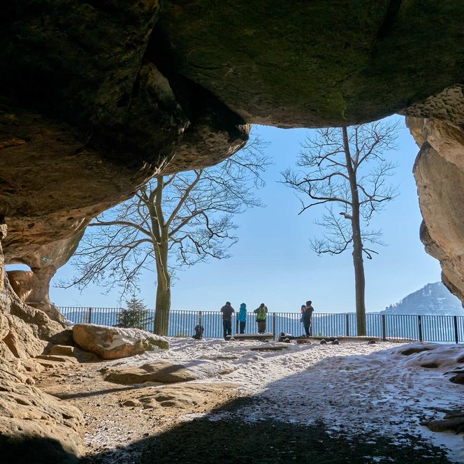 Blick aus einer Höhle auf eine Landschaft mit Bäumen und einer Gruppe von Menschen im Hintergrund.
