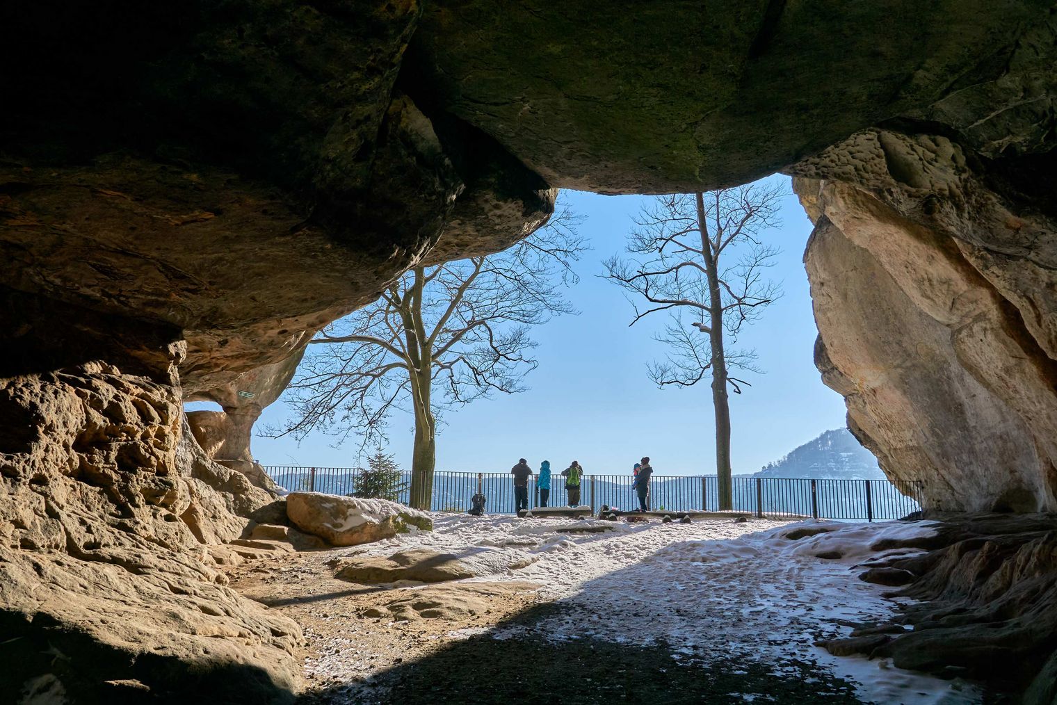 Blick aus einer Höhle auf eine Landschaft mit Bäumen und einer Gruppe von Menschen im Hintergrund.