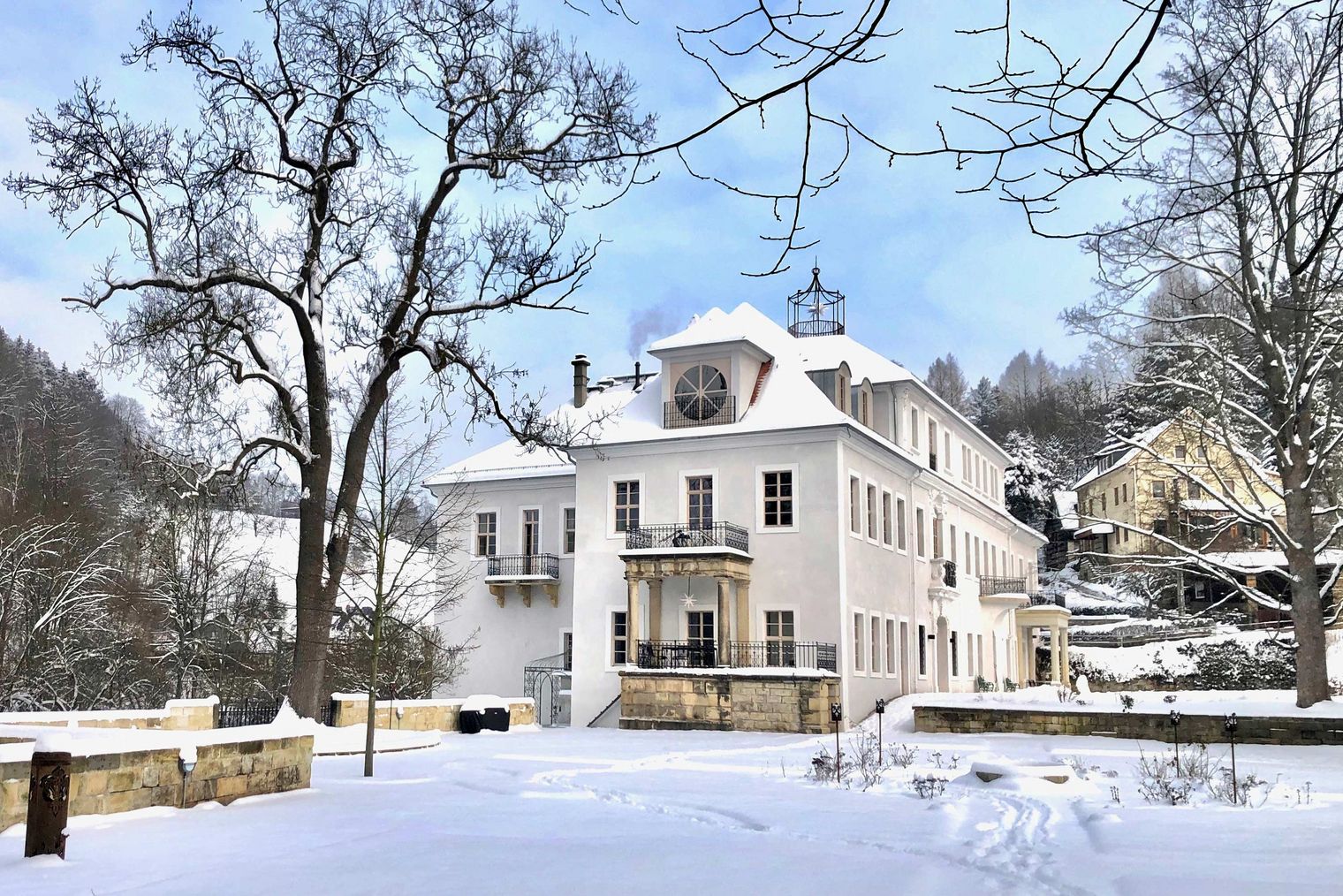 Historisches Gebäude mit Uhrturm, umgeben von Schnee und Bäumen.