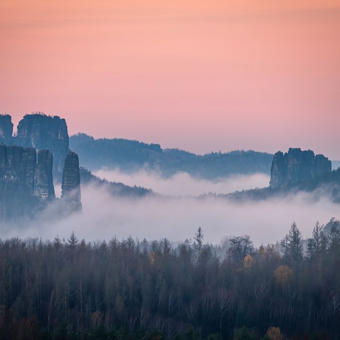 Felsenlandschaft mit Nebel und sanften Hügeln bei Sonnenaufgang, in sanften Rosa- und Blautönen.