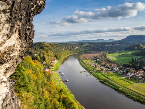 Blick auf Elbe bei Rathen, Felsen, grüne Wälder und blauer Himmel im Hintergrund.