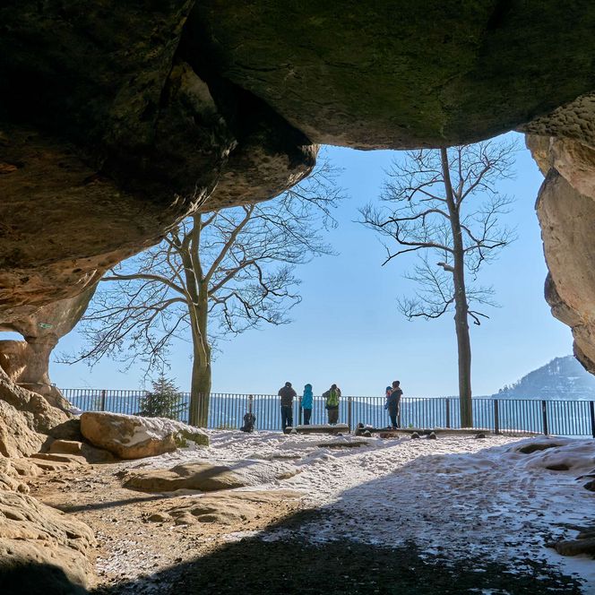 Blick aus einer Höhle auf eine Landschaft mit Bäumen und Menschen an einer Aussicht.